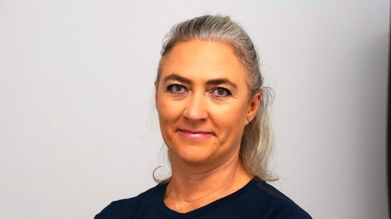 Firmeninhaberin Frau mit grauen langen Haaren und lächelndem Gesicht vor neutralem Hintergrund.